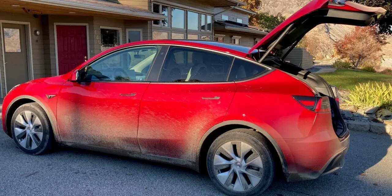 Red Tesla Model Y with road grime and dust caked along the lower doors and wheels, before a mobile detail